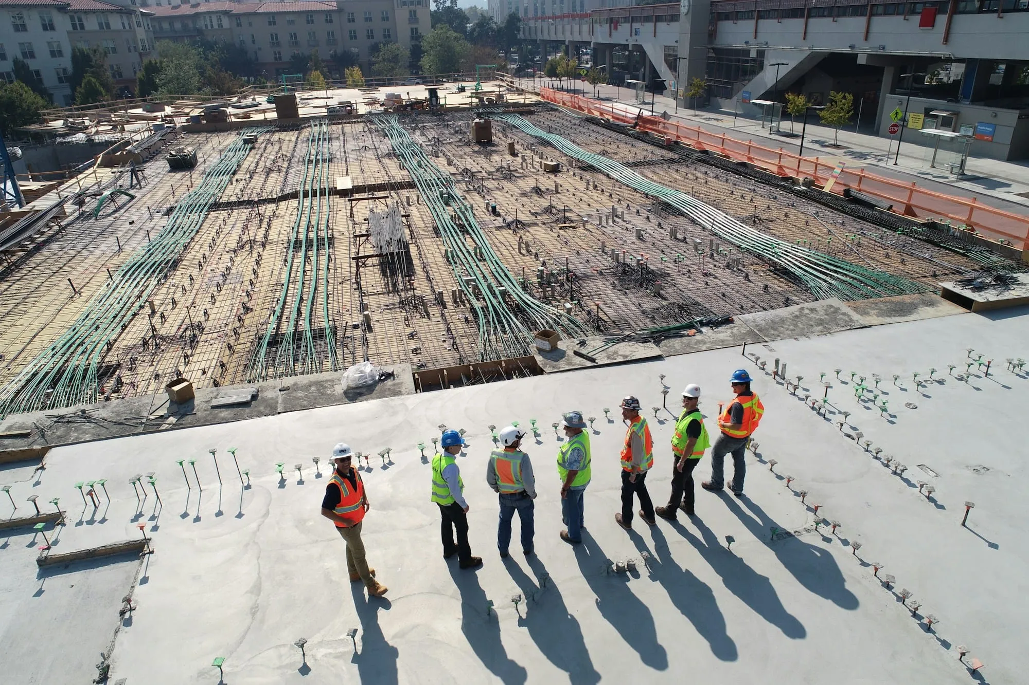 Seven workers in hard hats and vests on a concrete deck, seen from above
