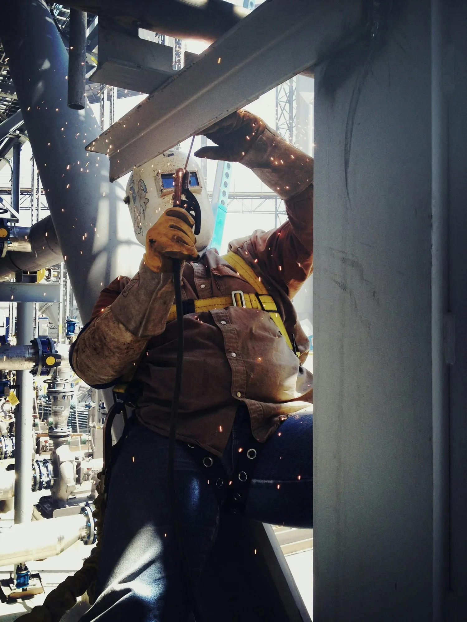 A welder in a safety harness working overhead as sparks fall